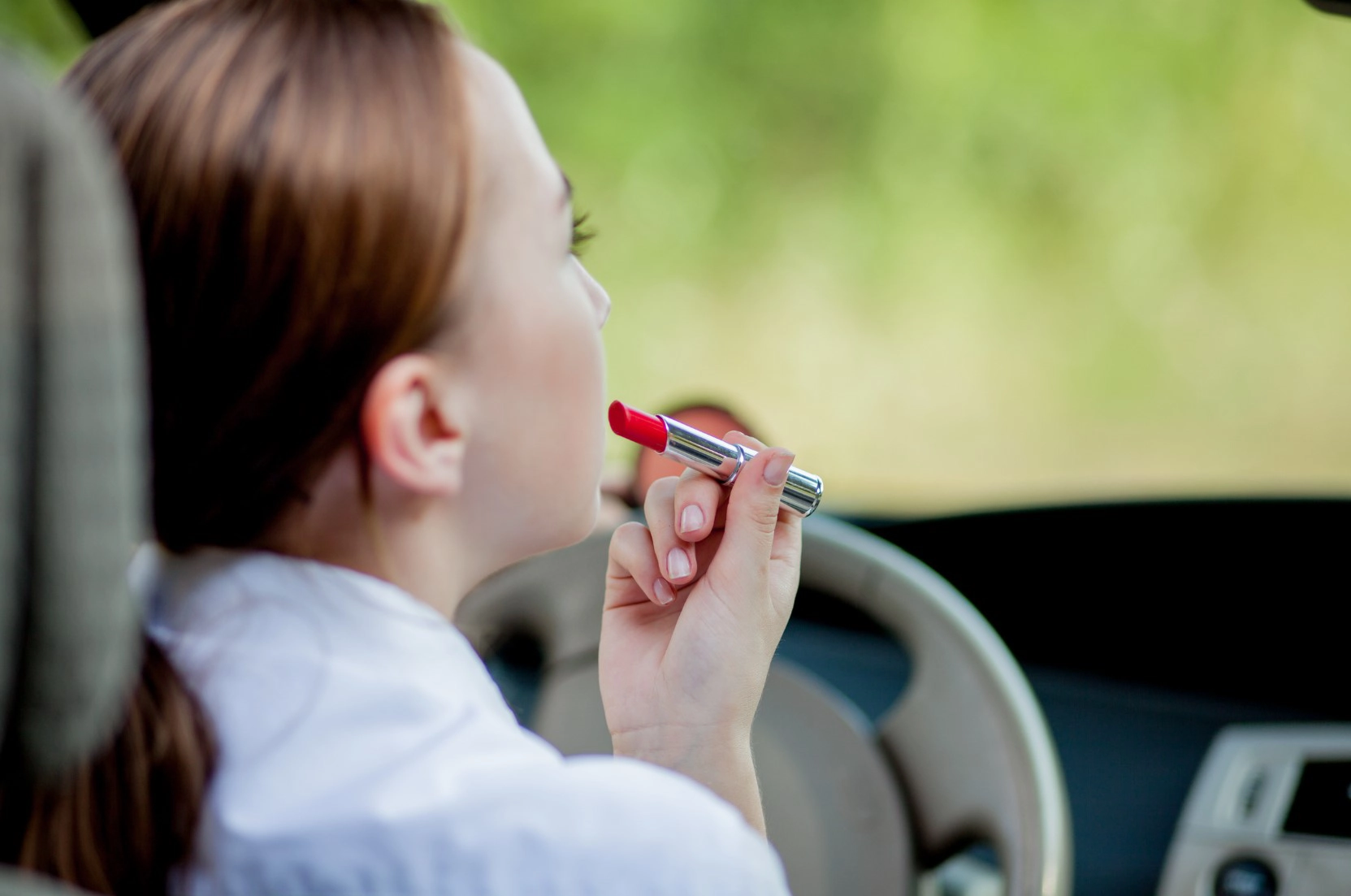 Woman applying lipstick while sitting behind the wheel of a car in Greensboro, NC, representing distracted or careless driving behavior.